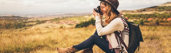 A young woman with a camera sitting in a medow taking pictures