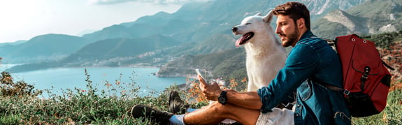 young man with his dog sitting on the side of a mountain