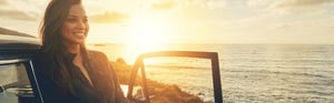 young woman leaning against her car looking out at the ocean