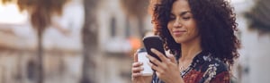 A young woman is walking on a city street, looking at her smartphone.