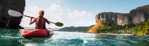 young woman kayaking in a river with cliffs in the background