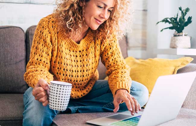 a woman sitting on a couch drinking coffee and browsing a laptop